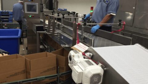 image inside a manufacturing plant of a conveyor belt with a worker next to it