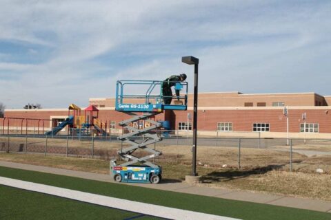 Decker Electric technician on a crane working on outdoor lighting at a high school sports field